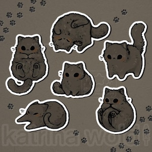 May include: A collection of seven cartoon cat stickers in various poses. The cats are dark gray with white outlines and small pink accents. Paw prints are scattered around the stickers on a gray background. The artist's name, "katrina wolf", is at the bottom.
