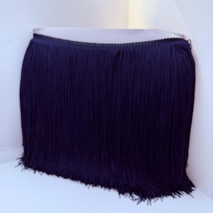 May include: A dark navy blue fringe trim featuring a woven header band with a delicate scalloped edge. The trim consists of long, straight, vertical strands of thread that hang down uniformly, creating a dense and textured appearance.