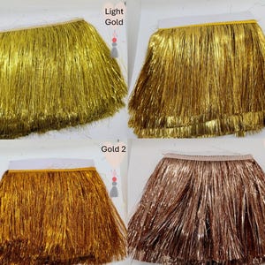 May include: Four rectangular swatches of metallic fringe trim arranged in a grid. The top left is labelled Light Gold, top right is Gold, bottom left is Gold 2, and bottom right is Rose Gold. Each swatch features long, thin, shiny strands.
