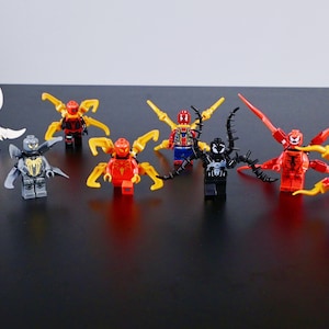 Peut inclure: Une collection de sept figurines en plastique sur le thème des super-héros, dotées de membres articulés, d'ailes amovibles et d'appendices mécaniques dans des tons de rouge, bleu, noir, blanc, jaune et gris.