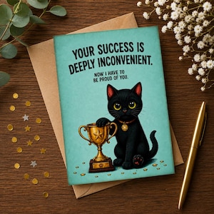 Może przedstawiać: Kartka okolicznościowa z turkusowym tłem przedstawiająca czarnego kota siedzącego obok złotego pucharu. Tekst brzmi: YOUR SUCCESS IS DEEPLY INCONVENIENT. NOW I HAVE TO BE PROUD OF YOU. Kot ma na sobie złotą obrożę z zawieszką w kształcie gwiazdki.