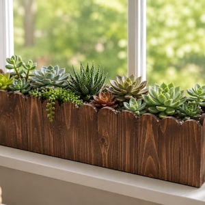 Puede incluir: Una jardinera rectangular de madera marrón oscuro con un borde superior festoneado, llena de una variedad de plantas suculentas verdes y de color marrón rojizo. La jardinera está colocada horizontalmente, mostrando una veta de madera natural y listones verticales.