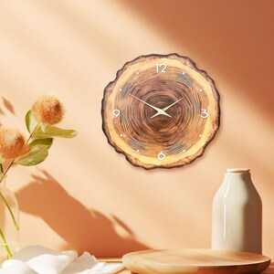 May include: A round wall clock featuring a natural wood slice design with visible grain patterns and bark edges. The clock face displays white numerals at the 12, 3, 6, and 9 o'clock positions, complemented by thin, gold-coloured metal clock hands.