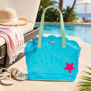 Peut inclure: Un sac fourre-tout bleu vif translucide en forme de coquillage avec des anses vert clair et un motif d'étoile de mer rose. Le sac présente un bord supérieur festonné et une petite plaque rectangulaire dorée avec le texte LUNA au centre.