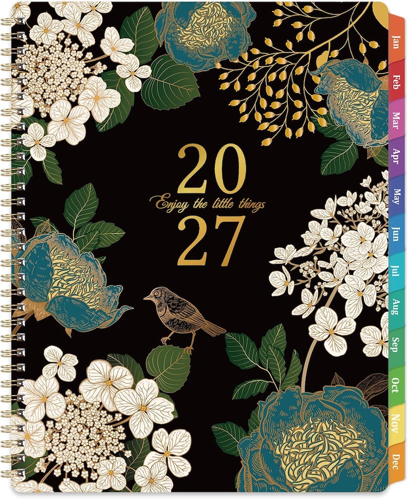 May include: A 2027 spiral-bound planner with a black cover featuring gold text that reads 2027 and Enjoy the little things. The design includes illustrations of white hydrangea flowers, teal and gold peonies, green leaves, and a small brown bird.