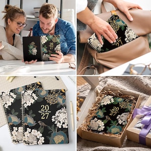 May include: A 2027 spiral-bound planner with a black cover featuring a floral pattern in teal, white, and gold, along with a small bird illustration and the text "20 27 Enjoy the little things" printed in gold on the front cover.