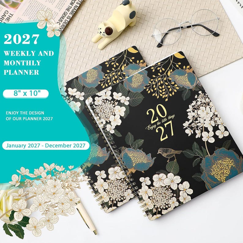 May include: A 2027 weekly and monthly planner measuring 20.32 cm by 25.4 cm, featuring a black cover with white and teal floral illustrations, gold text reading 2027 and Enjoy the little things, and a spiral binding for January to December.