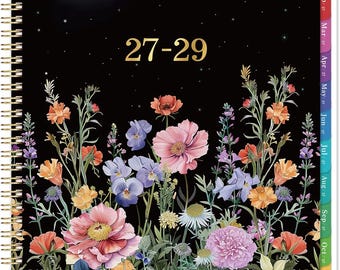 May include: A spiral-bound planner with a black cover featuring a night sky with a moon and stars above a vibrant field of colourful wildflowers. The text 27-29 is printed in gold in the centre. The side has colourful monthly index tabs.