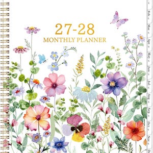 May include: A spiral-bound monthly planner with a white cover featuring a watercolor illustration of various colorful wildflowers, green foliage, and a small butterfly. The text 27-28 MONTHLY PLANNER is printed in gold. It includes monthly side tabs.