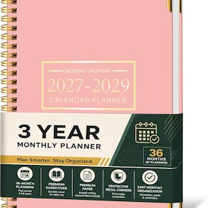 May include: A pink 3-year monthly calendar planner for 2027-2029 with a gold spiral binding and gold-tone metal corner protectors. The cover features a white and gold rectangular label with text and a dark green belly band with white icons.