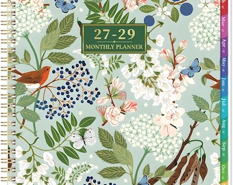 May include: A spiral-bound monthly planner with a light green cover featuring a botanical illustration of white flowers, dark blue berries, brown birds, and butterflies. The centre text reads 27-29 MONTHLY PLANNER. It includes coloured monthly tabs.
