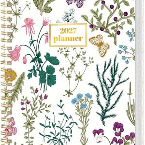 May include: A 2027 planner with a white cover featuring a botanical illustration of various green plants, colorful flowers, and butterflies. The planner is bound with a gold-colored metal spiral coil on the left side and includes the text 2027 planner.