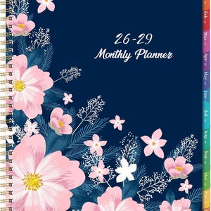 May include: A navy blue monthly planner with a gold spiral binding, featuring a floral pattern of pink flowers and dark blue foliage. The cover displays the white text 26-29 Monthly Planner and includes colored monthly tabs along the right edge.
