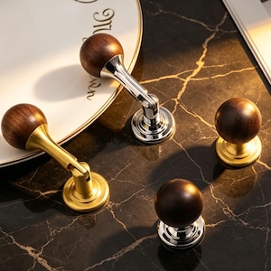 May include: A collection of four furniture knobs featuring spherical dark brown wooden heads. Two knobs have hinged metal arms in polished chrome and brushed brass finishes, while two are stationary knobs with matching chrome and brass circular bases.
