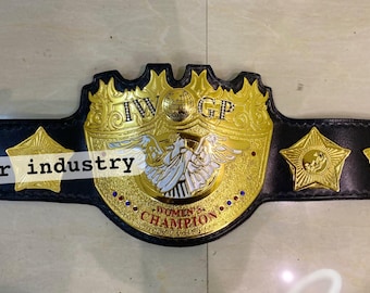 May include: A black leather championship belt featuring a large central gold-colored metal plate with the text IWGP and WOMEN'S CHAMPION, an eagle emblem, and small red and blue accents. Four gold star-shaped side plates are attached to the strap.