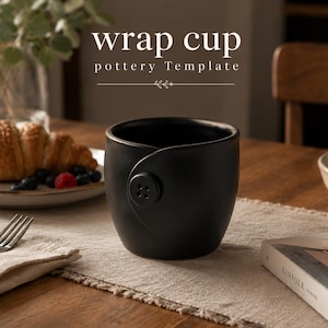 May include: A matte black ceramic cup featuring a wrap-around design secured by a single circular button on the front. The text "wrap cup pottery Template" is displayed above the cup in a white serif font with a small decorative line element.