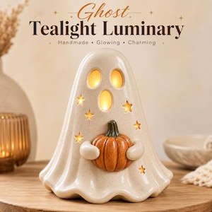 May include: A cream-colored ceramic ghost tealight luminary featuring cutouts for eyes and stars, holding a small orange pumpkin. The text "Ghost Tealight Luminary" is printed above the figure, which emits a warm, glowing light from within.