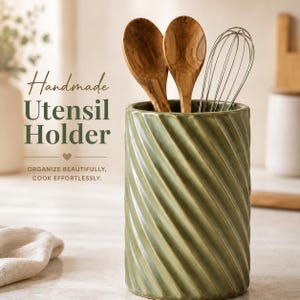 May include: A cylindrical sage green ceramic utensil holder with a diagonal ribbed texture. It contains two wooden spoons and a metal wire whisk. The text on the image reads: Handmade Utensil Holder, ORGANIZE BEAUTIFULLY, COOK EFFORTLESSLY.