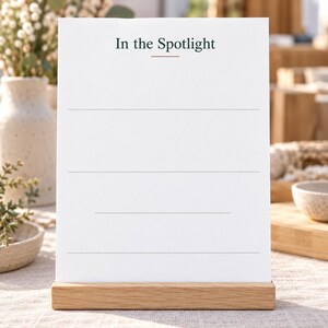 Op de afbeelding: Een wit rechthoekig bord met de tekst In the Spotlight in donkergroen bovenaan, een dunne horizontale oranje lijn onder de tekst en vier dunne horizontale grijze lijnen eronder om op te schrijven.