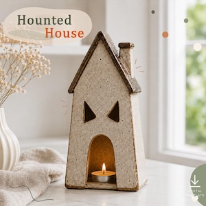 May include: A speckled beige ceramic house-shaped candle holder with a dark brown roof and chimney. The structure features two triangular cut-out windows and an arched doorway containing a lit tea light candle. The text Haunted House is visible.