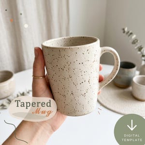 Puede incluir: Una taza de cerámica cónica con un acabado crema moteado y un asa curva. La taza presenta un borde liso ligeramente acampanado y una superficie texturizada con motas de color marrón oscuro. El texto Tapered Mug es visible.