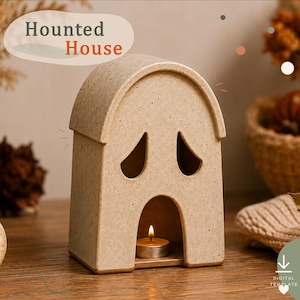 Può includere: Un portacandele in ceramica beige maculato a forma di fantasma con una parte superiore arcuata, due aperture per gli occhi a forma di lacrima e una grande apertura arcuata alla base contenente un lumino acceso. Il testo Haunted House è visibile.