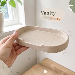 May include: An oval-shaped vanity tray in a speckled beige colour with a smooth finish and a small notch on the front rim. The text "Vanity Tray" is printed in the upper right corner, along with a download icon and the words "Digital Template".