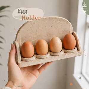 May include: A speckled beige egg holder with a semi-circular back panel and four circular indentations, each holding a brown egg. The text "Egg Holder" and "DIGITAL TEMPLATE" are visible on the image, indicating a design for crafting.