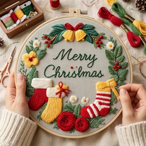 May include: A circular embroidery hoop containing a gray fabric panel with the embroidered text Merry Christmas. The design features a wreath of green leaves, red berries, yellow bells, white flowers, and three stockings in red, yellow, and striped patterns.