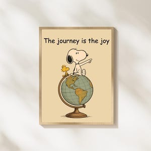 Könnte beinhalten: Ein rechteckiger Wanddruck auf hellbeigem Hintergrund mit einer Cartoon-Illustration von Snoopy und Woodstock, die auf einem Globus sitzen. Der Text "The journey is the joy" steht in Schwarz darüber. Der Globus hat einen braunen Ständer.