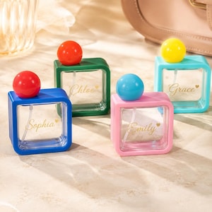 May include: Four square glass perfume bottles with colourful frames and spherical caps. The blue bottle is labelled Sophia, the green bottle is labelled Chloe, the pink bottle is labelled Emily, and the light blue bottle is labelled Grace in gold script.
