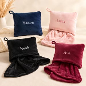 Peut inclure: Quatre couvertures pliables rectangulaires en peluche avec poignées de transport. Les couvertures sont bleu marine, rose clair, noir et rouge foncé, chacune brodée d'un prénom : Mason, Luna, Noah et Ava. Le tissu doux a une texture duveteuse.