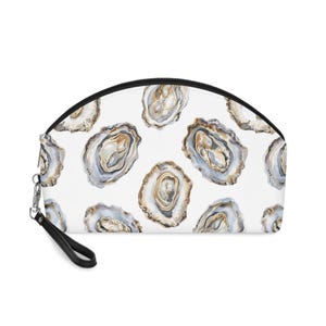 Könnte beinhalten: Eine halbkreisförmige Tasche mit einem sich wiederholenden Aquarellmuster aus Austernschalen in Weiß-, Grau- und Beigetönen auf weißem Grund. Die Tasche verfügt über einen schwarzen Reißverschluss an der Oberkante und eine schwarze Handschlaufe.