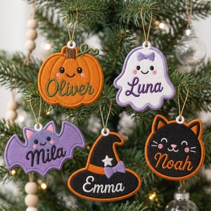 May include: Five embroidered felt ornaments featuring Halloween characters: an orange pumpkin labeled Oliver, a white ghost with a bow labeled Luna, a purple bat labeled Mila, a black witch hat labeled Emma, and a black cat labeled Noah.