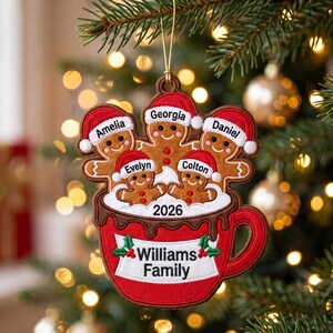 May include: A Christmas tree ornament shaped like a red mug filled with five gingerbread figures wearing Santa hats. The figures are personalised with the names Amelia, Georgia, Daniel, Evelyn, and Colton. The mug features the text Williams Family and 2026.
