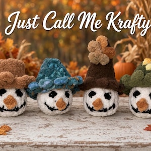 May include: Four crocheted plush figures with white round bodies, black stitched eyes and mouths, and orange noses. Each figure wears a unique textured hat in brown, blue, dark brown with pom-poms, or green. The text Just Call Me Krafty is visible.