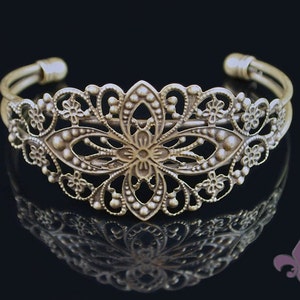 May include: A silver-toned metal bracelet with a delicate, floral design. The bracelet is open and adjustable.
