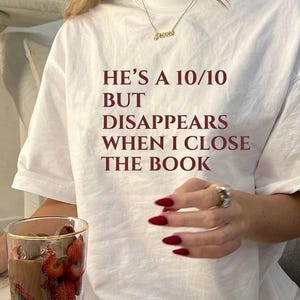 Può includere: Una t-shirt bianca a maniche corte con il testo rosso scuro HE'S A 10/10 BUT DISAPPEARS WHEN I CLOSE THE BOOK stampato sul davanti. La maglietta presenta un girocollo e una vestibilità rilassata, ideale per un look casual quotidiano.