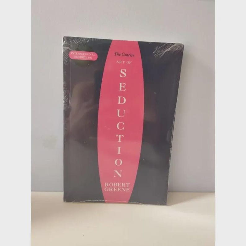 Pu&ograve; includere: Un libro intitolato The Concise Art of Seduction di Robert Greene, caratterizzato da una copertina nera con un grande ovale rosa verticale al centro contenente il testo bianco Seduction e una piccola etichetta rosa International Bestseller nell'angolo.