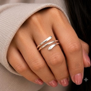 May include: A polished silver-tone ring featuring a bypass design with two overlapping bands that wrap around the finger. The metal has a smooth, reflective surface with rounded, tapered ends, creating a continuous spiral appearance on the finger.