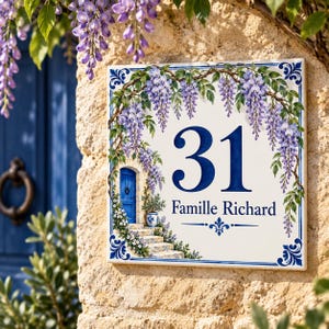 Könnte beinhalten: Ein quadratisches Keramik-Hausschild mit der Nummer 31 und dem Text Famille Richard in dunkelblauer Schrift. Das Design zeigt eine gemalte Illustration einer blauen Tür, Steinstufen und hängenden violetten Glyzinien mit grünen Blättern.