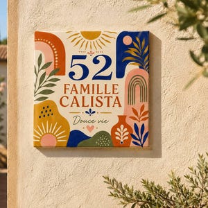 Peut inclure: Une plaque de maison carrée en céramique sur fond crème affichant le numéro 52, le texte FAMILLE CALISTA et la mention Douce vie. Le motif présente des formes abstraites colorées, des arches, des soleils et des illustrations botaniques en bleu, orange, rose et jaune.