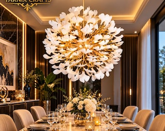 May include: A spherical chandelier featuring numerous white ginkgo leaf-shaped accents attached to a gold-toned metal frame. The fixture is suspended from the ceiling and illuminates a dining area. The text TARNIX CRAFTS is visible.