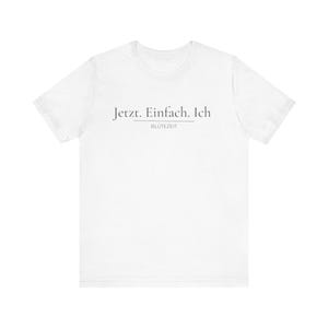 May include: A white short-sleeved t-shirt featuring the dark grey text "Jetzt. Einfach. Ich" printed on the chest, with the word "BLÜTEZEIT" positioned directly underneath the text, separated by a thin horizontal line centred on the front.