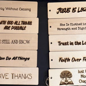 May include: Ten rectangular light-colored wooden bookmarks with laser-engraved text and designs. Each bookmark features a small hole on the left side. The phrases include Pray Without Ceasing, With God All Things Are Possible, Be Still And Know, I Can Do All Things, Give Thanks, Jesus Is Lord, She Is Clothed In Strength And Dignity, Trust In The Lord, Faith Over Fear, and Just One More Chapter.