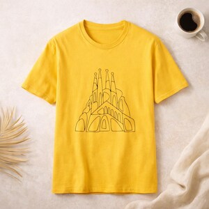 May include: A bright yellow short-sleeve t-shirt featuring a black line art graphic of the Sagrada Familia cathedral on the centre chest. The shirt has a classic crew neckline and a straight hem, constructed from a solid-coloured cotton fabric.