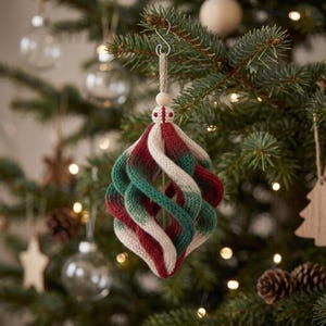 May include: A spiral-shaped Christmas ornament crafted from knitted fabric in alternating bands of cream, forest green, and deep red. The ornament features a central wooden bead at the top, suspended by a jute twine loop and a silver metal hook.