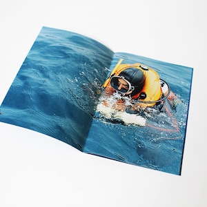 Può includere: Un subacqueo con una muta da subacquea gialla e nera nuota in acqua blu.