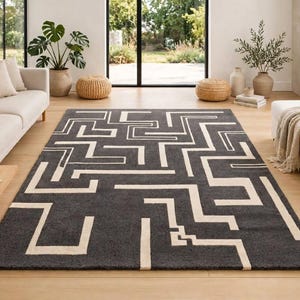 May include: A rectangular area rug featuring a dark charcoal gray background with a contrasting cream-colored geometric pattern of interconnected lines that form a maze-like design across the entire surface of the floor covering.