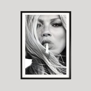 May include: A black and white framed wall art print featuring a close-up portrait of a person with long hair partially obscuring their face. The person is holding a lit cigarette between their lips, with a thin trail of smoke rising upwards.